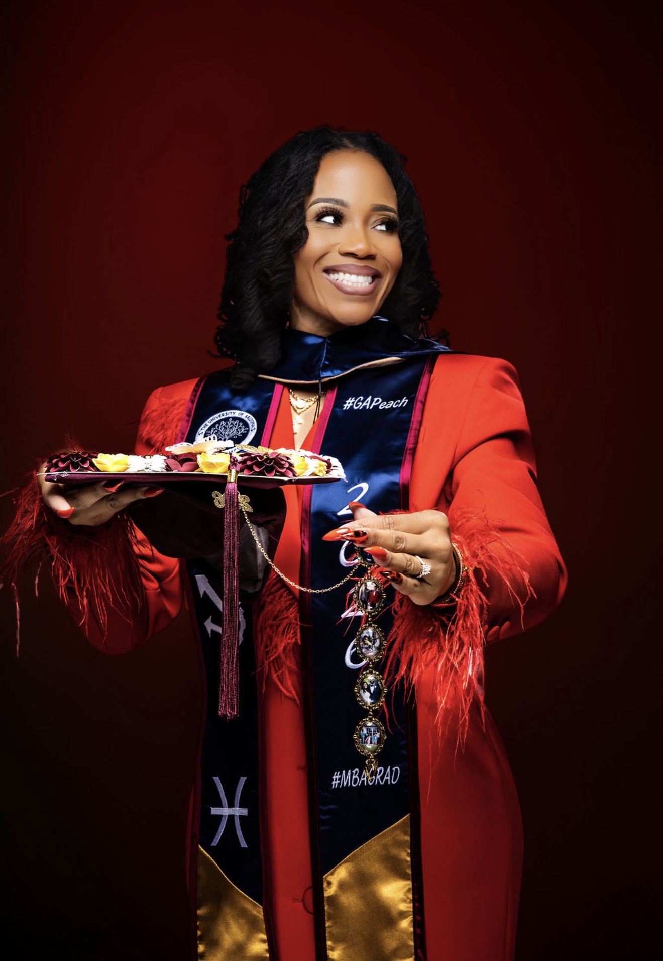 Leonia Moore smiling in red academic regalia while holding her graduation cap